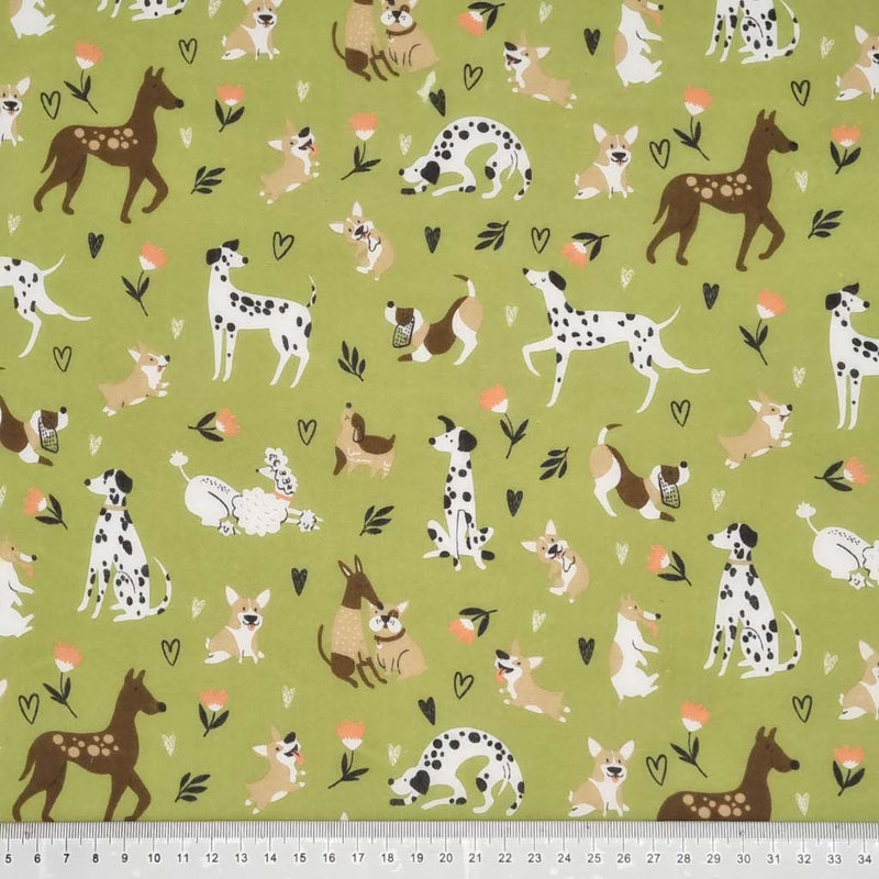 Various breeds of dogs playing are printed on an olive green polycotton fabric with a cm ruler