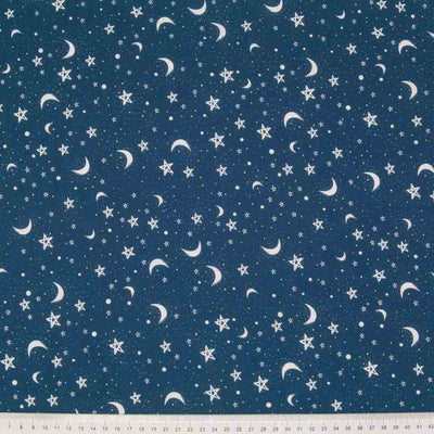 Small white stars and moons are printed in clusters on a blue polycotton fabric with a cm ruler at the bottom