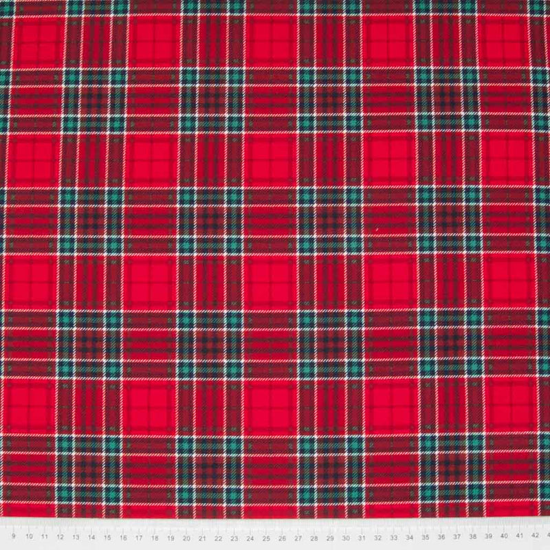 A 100% cotton christmas tartan plaid fabric with a dominant colour of red with a cm ruler at the bottom