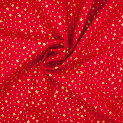 A red christmas cotton fabric featuring small metallic gold stars in a tossed pattern in a decorative swirl