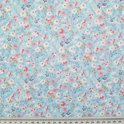 White, pink and blue ditsy flowers are printed on a sky blue polycotton fabric with a ruler at the bottom for size perspective
