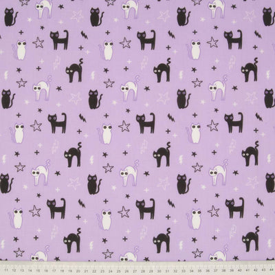 Black cats, stars and lightning bolts are printed on a lilac polycotton fabric with a cm ruler at the bottom