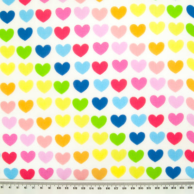 Lines of brightly coloured hearts are printed on a fat quarter of white polycotton fabric with a ruler at the bottom for size perspective