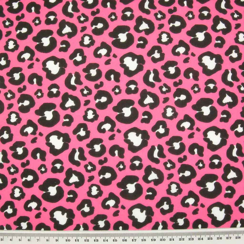 White and black leopard spots printed on a bright pink polycotton fabric with a ruler for size perspective