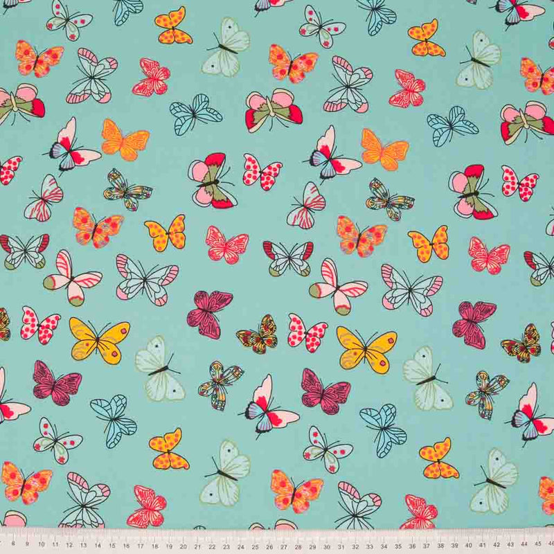 Pink and orange butterflies printed on a dark mint cotton poplin fabric by Rose & Hubble with a cm ruler at the bottom