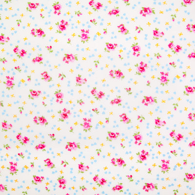 Small, single scattered pink roses with tiny blue hearts and ochre bows printed on a white Rose and Hubble cotton fabric pictured flat