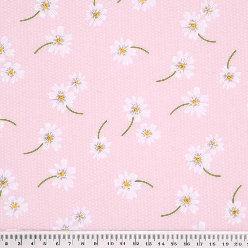 White daisies in a scattered pattern are printed on a pink polycotton fabric with tiny white spots with a cm ruler