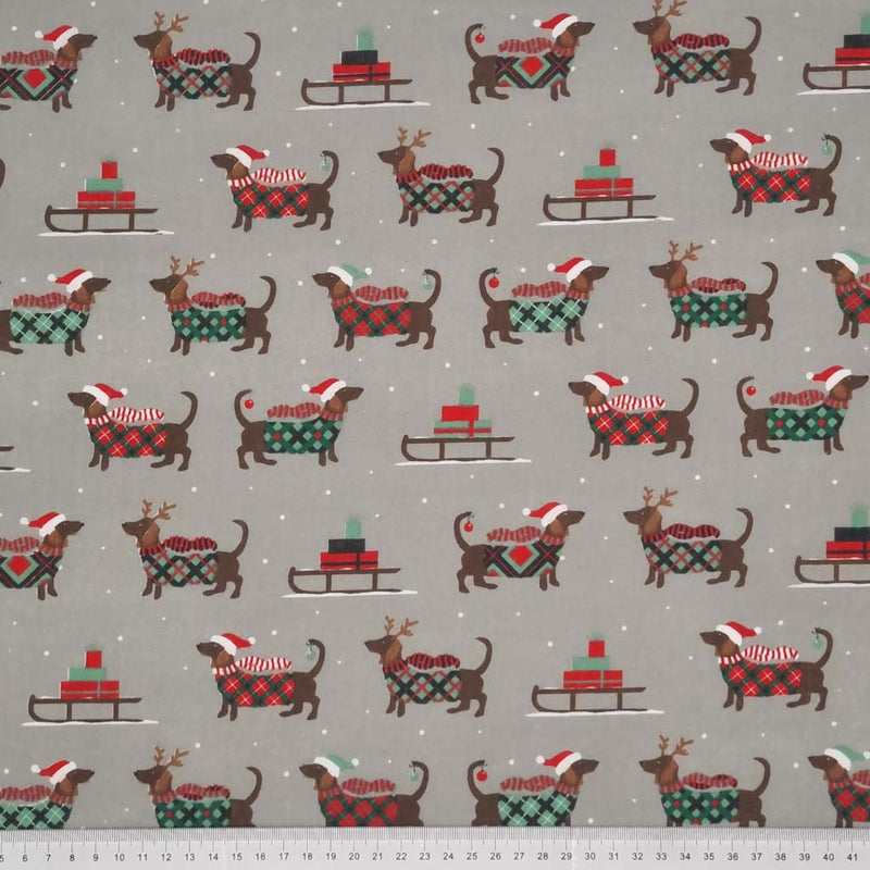 cute dachshund sausage dogs wearing Christmas jumpers and sledges laden with gifts are printed on a silver polycotton fabric with a cm ruler at the bottom