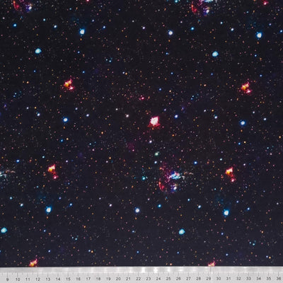 A digitally printed 100% black cotton fabric is adorned with coloured stars and meteors with a cm ruler at the bottom
