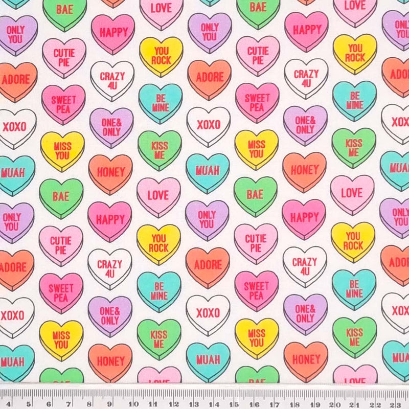 Colourful candy love hearts printed on a white cotton fabric with a cm ruler at the bottom