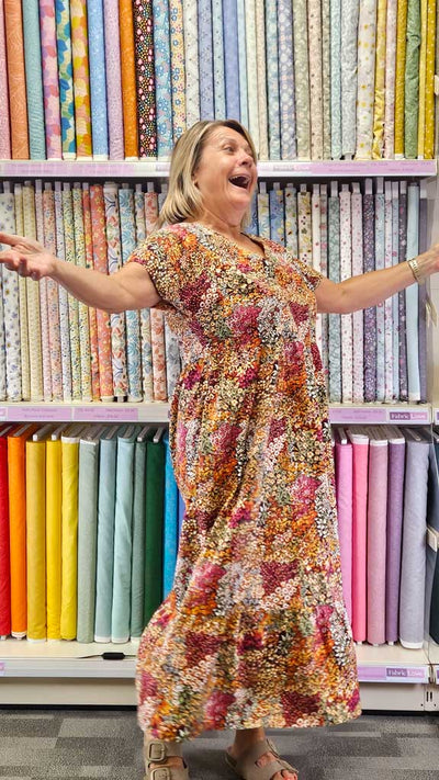 Woman in a colorful dress standing in front of fabric shelves with various patterns and colors.