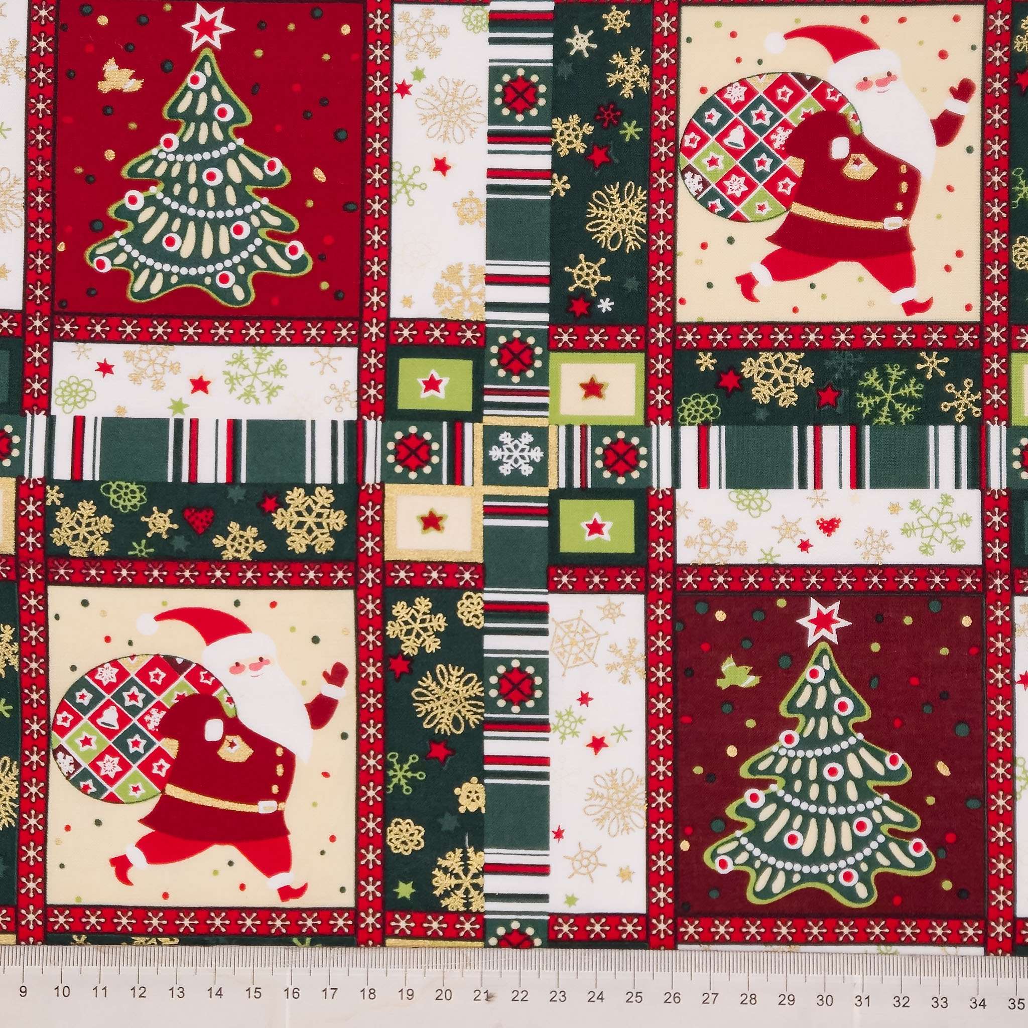 A close-up of a Christmas-themed fabric pattern featuring four large panels with Santa Claus and decorated Christmas trees, surrounded by striped borders and snowflake motifs. A measuring ruler is visible along the bottom edge.