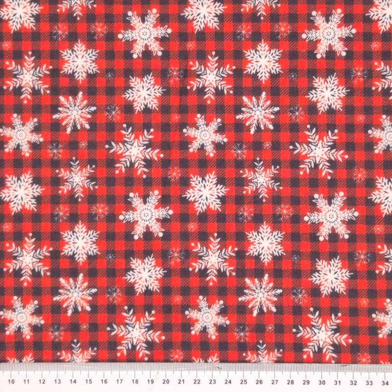 Snowflakes printed on a red and black check polycotton fabric with a cm ruler