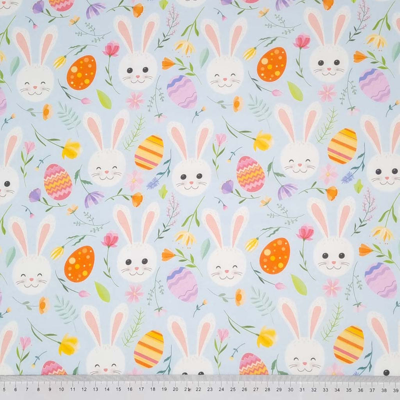 Easter fabric with bunny faces and easter eggs on a pastel blue cotton fabric with a cm ruler