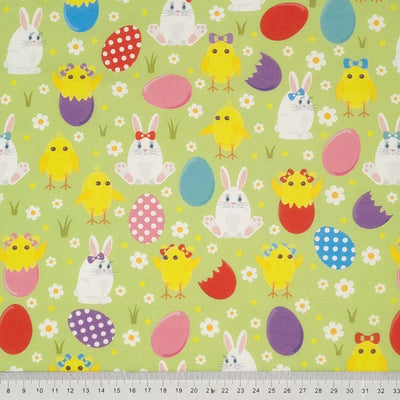 Easter bunnies, chicks and eggs are printed on a pastel green cotton fabric by Rose & Hubble with a cm ruler
