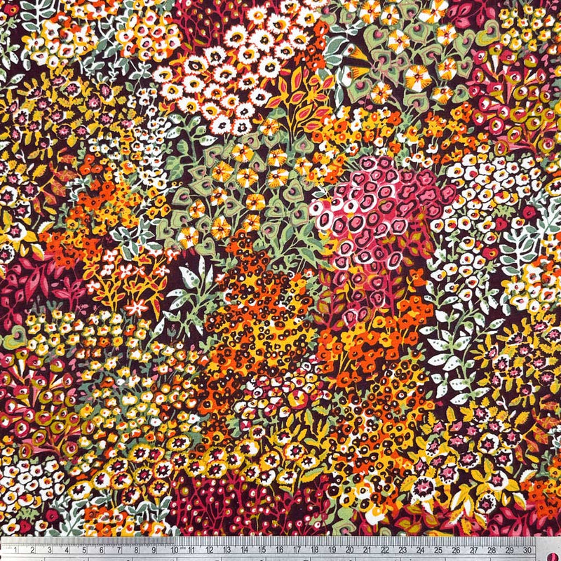 Intricate wildflowers and vines, in summer shades of orange, pink and yellow, printed on a deep black 100% cotton fabric with a cm ruler