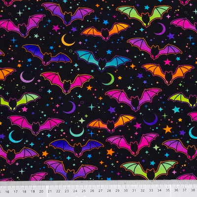 Neon pink and blue flying bats and stars are printed on a black cotton jersey fabric with a cm ruler