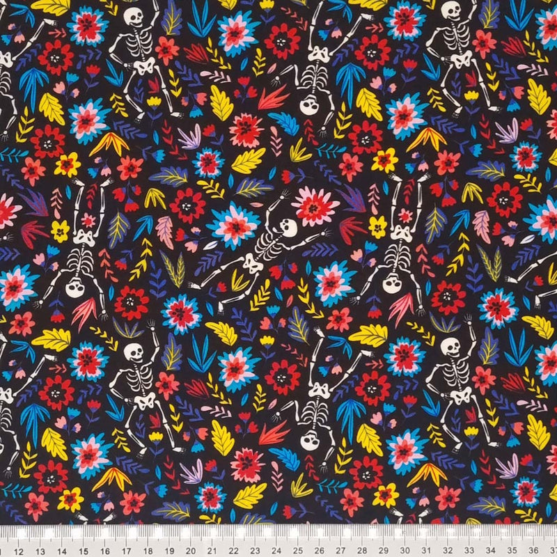 Skeletons and bright flowers are printed on a black cotton poplin fabric by Rose & Hubble with a cm ruler