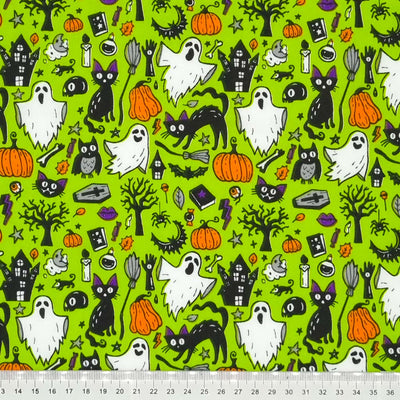 Ghosts, cats and pumpkins are printed on a green halloween polycotton fabric with a cm ruler