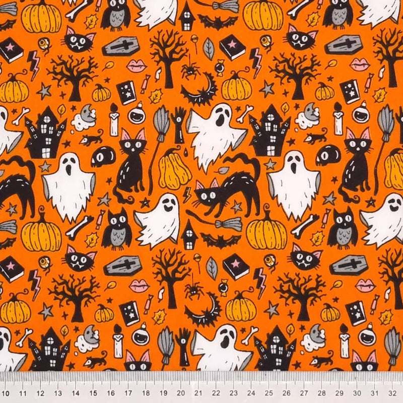Ghosts, cats and pumpkins are printed on an orange halloween polycotton fabric with a cm ruler