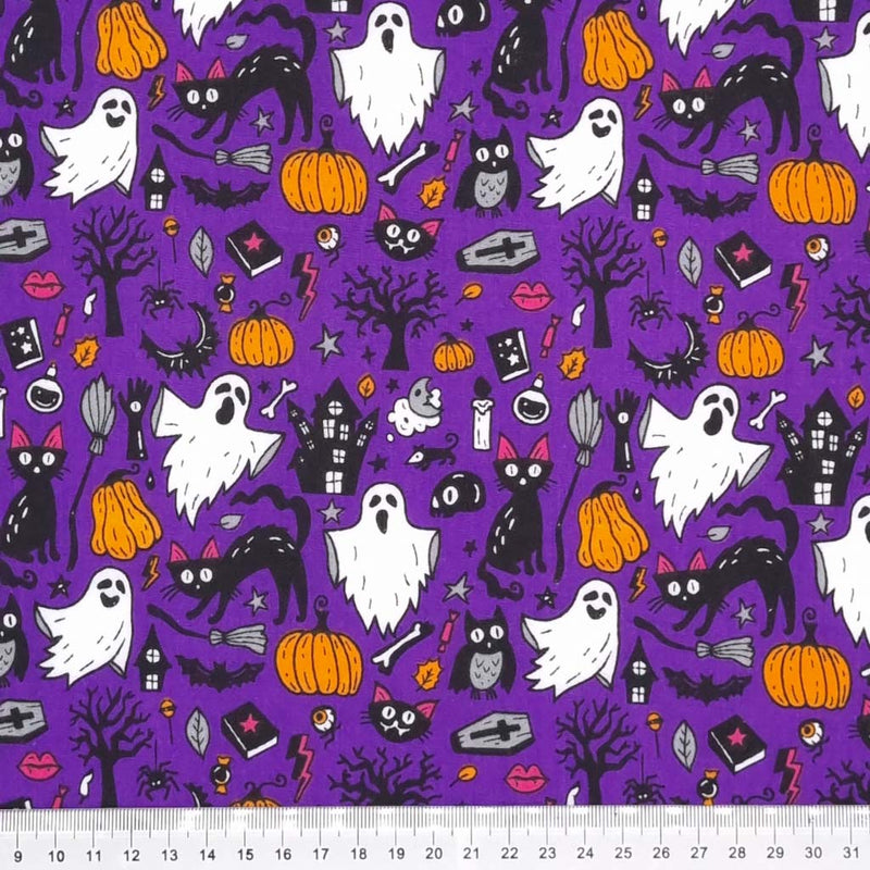 Ghosts, cats and pumpkins are printed on a purple Halloween polycotton fabric with a cm ruler