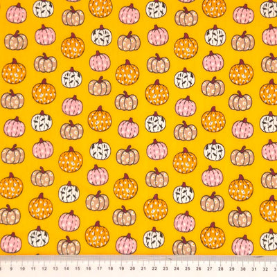 Ditsy decorated pumpkins are printed on an orange polycotton fabric for halloween with a cm ruler