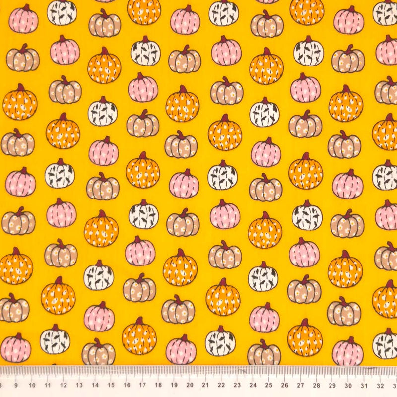 Ditsy decorated pumpkins are printed on an orange polycotton fabric for halloween with a cm ruler