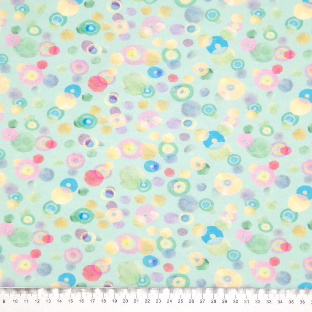 Pastel coloured spots printed on an aqua cotton jersey fabric with a cm ruler