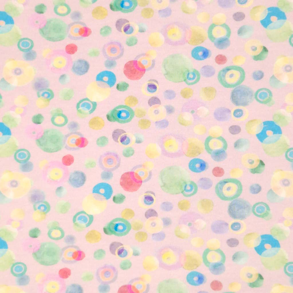 Pastel coloured spots printed on a pale pink cotton jersey fabric flat.