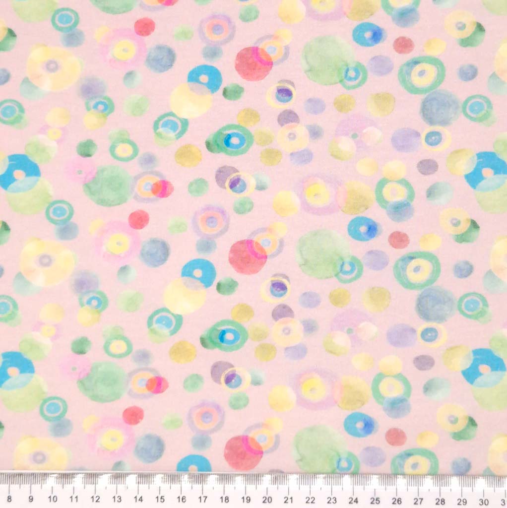 Pastel coloured spots printed on a pale pink cotton jersey fabric with a cm ruler
