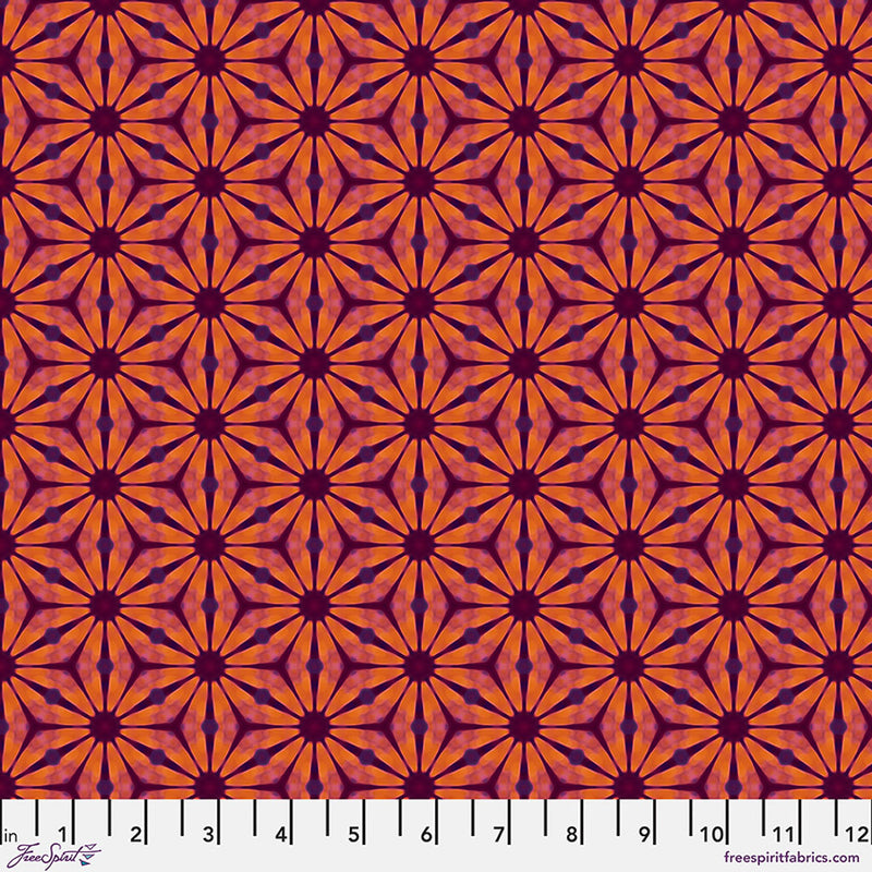 A floral geometric pattern in reds and oranges printed on a cotton quilting fabric with a cm ruler