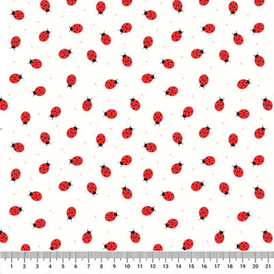 Miniature ladybirds scrambling across a white cotton fabric with a cm ruler