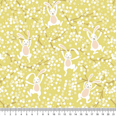 Bouncing Easter bunnies jumping in the spring blossom printed on a yellow cotton fabric with a cm ruler