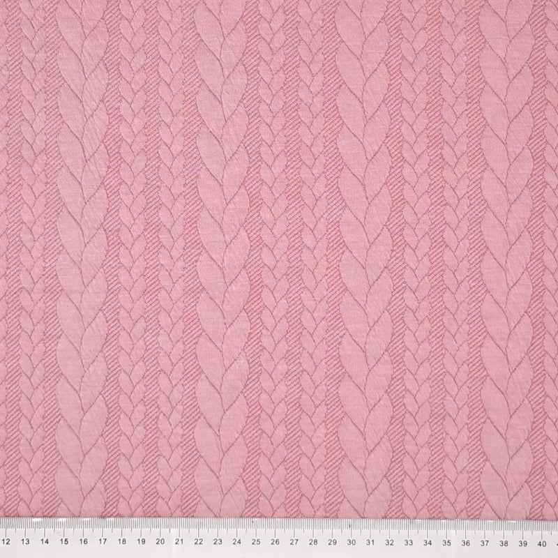 A rose pink coloured cable knit fabric with a cm ruler