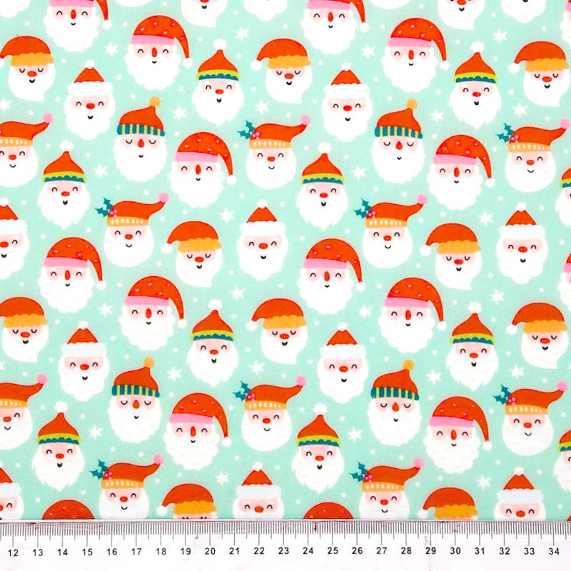 Pattern of cartoon Santa Claus faces with colorful hats on a light blue polycotton fabric, with a ruler at the bottom.