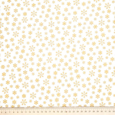 Pattern of gold snowflakes on a cream cotton fabric with a ruler at the bottom.