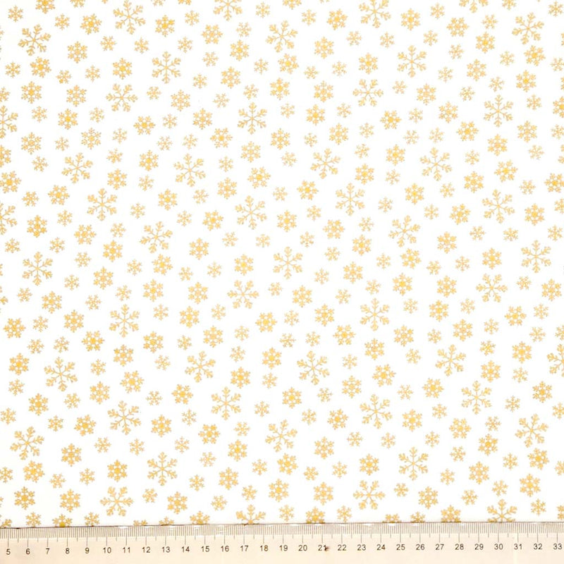 Pattern of gold snowflakes on a cream cotton fabric with a ruler at the bottom.