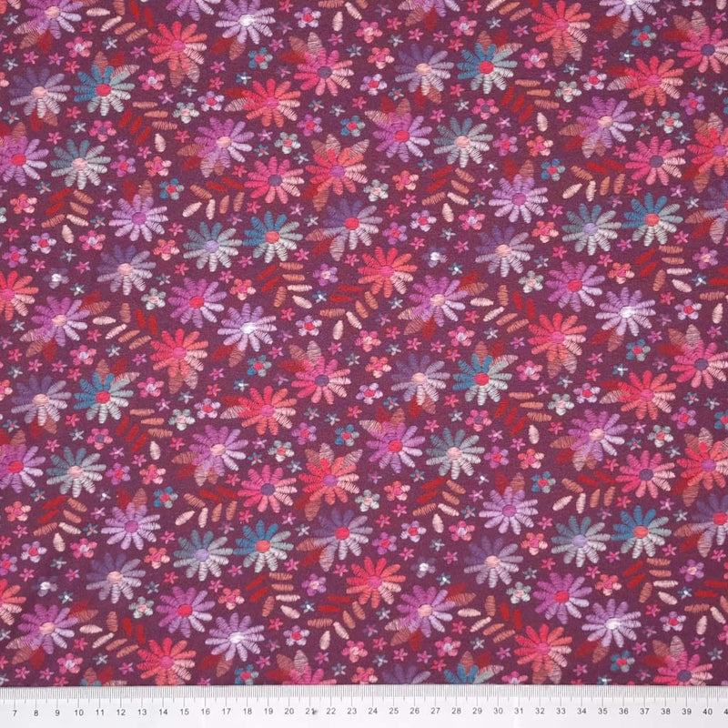 A mulberry coloured single cotton jersey fabric printed with embroidery look flowers with a cm ruler
