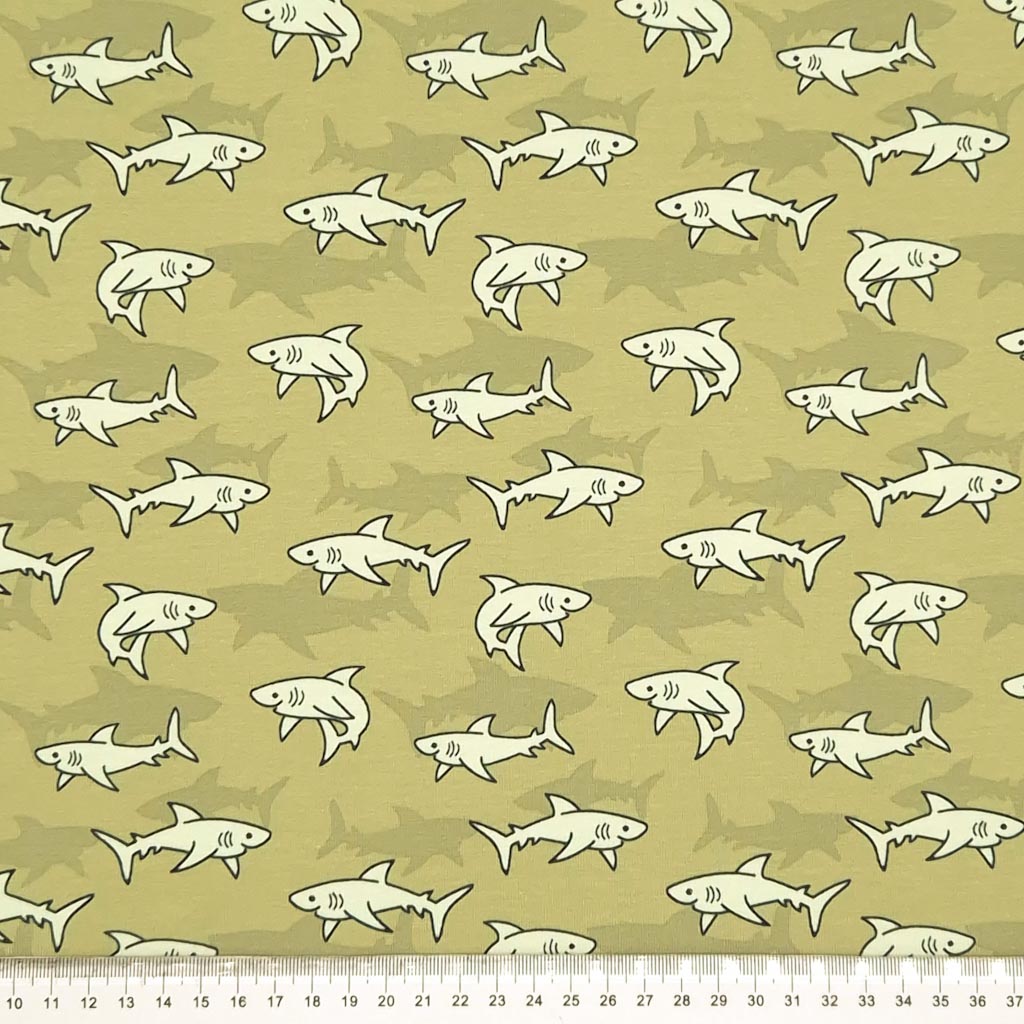 Swimming sharks are printed on a green cotton jersey fabric with a cm ruler