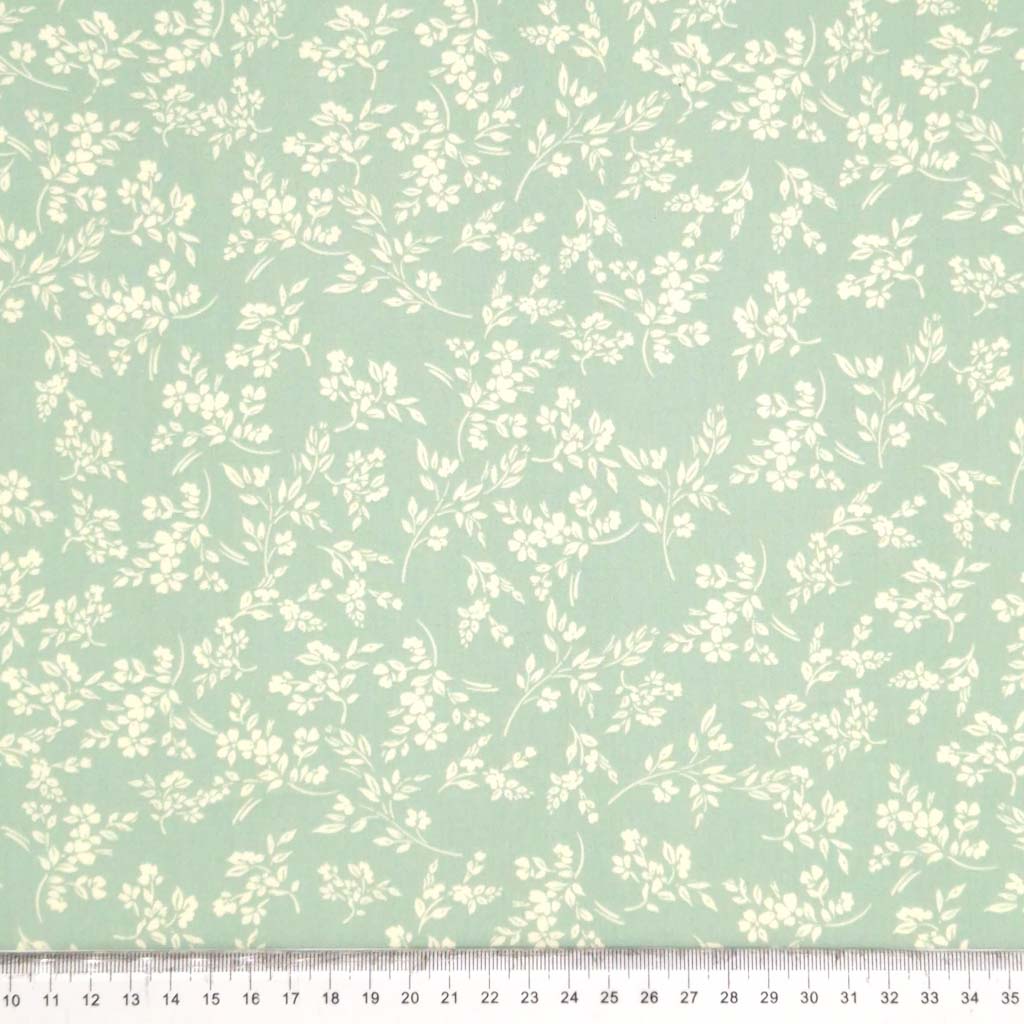 A cream vine floral printed on a sge green cotton poplin fabric by Rose & Hubble with a cm ruler