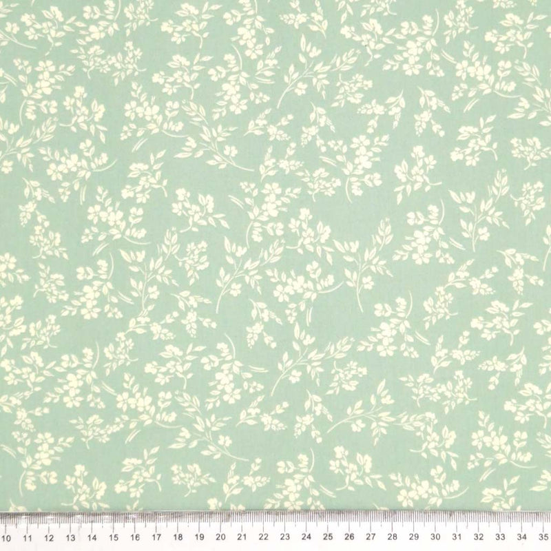 A cream vine floral printed on a sge green cotton poplin fabric by Rose & Hubble with a cm ruler