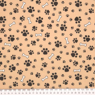 Dog paws and bones printed on a camel coloured polycotton fabric with a cm ruler