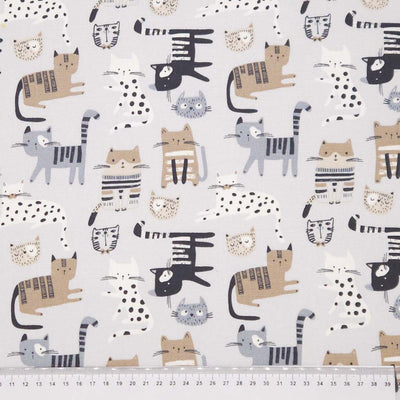 Pattern of cartoon cats  on a pale grey canvas fabric with a cm ruler