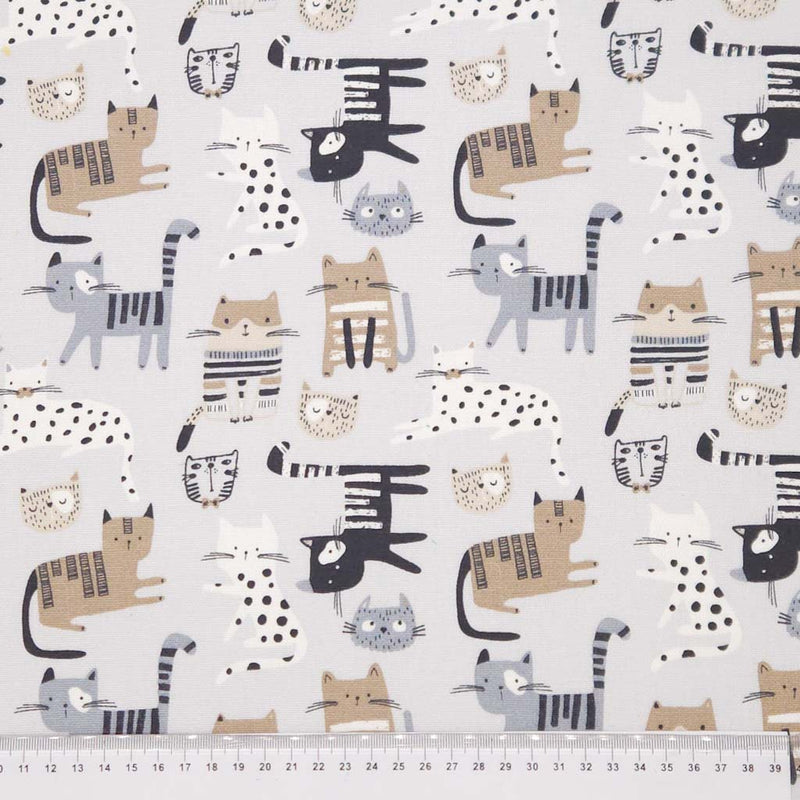 Pattern of cartoon cats  on a pale grey canvas fabric with a cm ruler