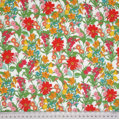 Vibrant red, orange and yellow flowers printed on a white cotton lawn fabric with a cm ruler
