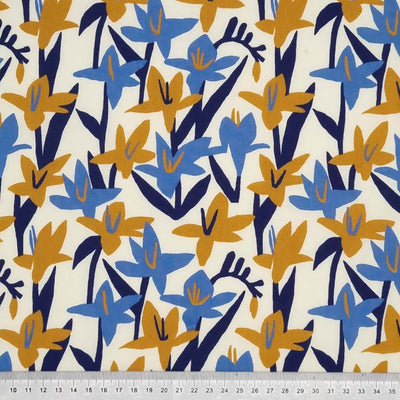 Blue and mustard Lily flowers are printed on a cream polycotton fabric with a cm ruler