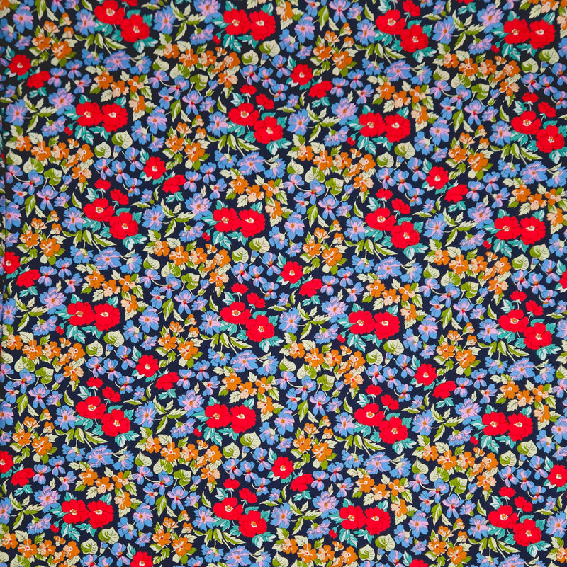 Navy blue pima cotton lawn fabric with a small floral pattern featuring red, orange, and blue flowers.