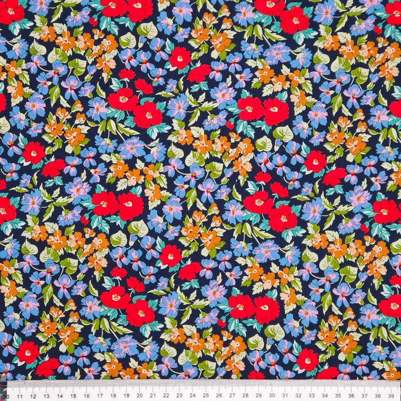 Colorful floral pattern on a dark blue pima cotton lawn fabric with a ruler at the bottom.