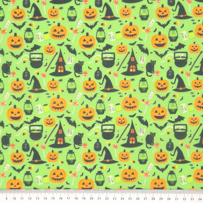 Halloween-themed fabric pattern with pumpkins, cats, and witches' hats on a green polycotton fabric with a cm ruler
