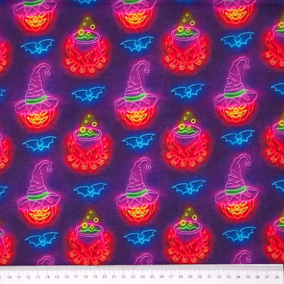 Neon Halloween-themed fabric pattern with pumpkins, cauldrons, and bats on a dark cotton fabric with a cm ruler.